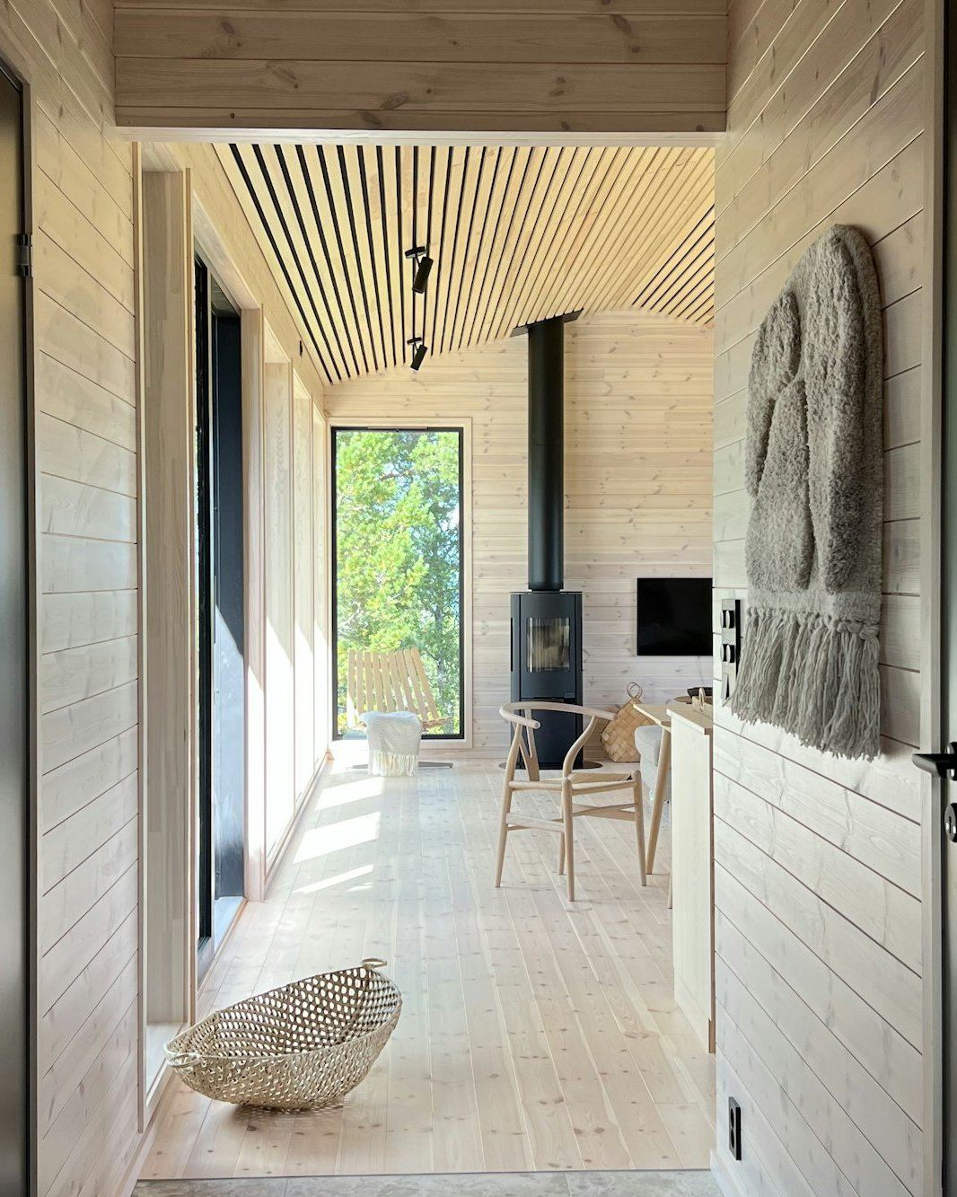 Innenraum mit heller Holzdecke, Kaminwand und Blick durch die geöffnete Tür ins Freie