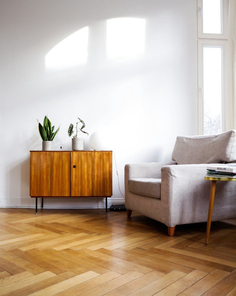 Wohnraum mit Fischgrätparkett, Sideboard und Sessel am Fenster